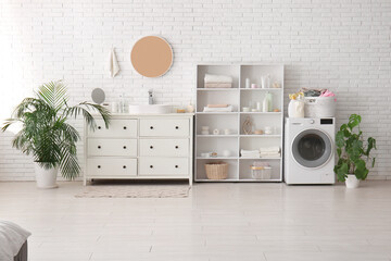 Modern washing machine, shelving unit and chest of drawers in interior of laundry room