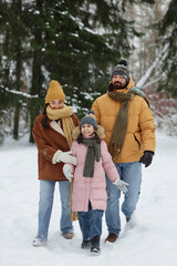 Vertical full length portrait of happy young family walking together in winter forest with daughter...