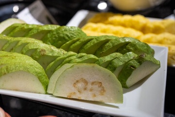 Fresh sliced guava and pineapple on a white platter, tropical fruit arrangement at a buffet.