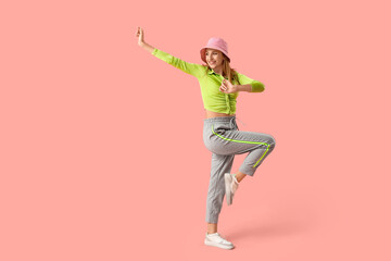 Beautiful young happy woman in stylish hat dancing on pink background