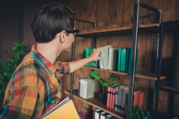 Photo of clever smart man wear checkered shirt choose book indoors college library