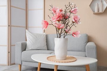 Cozy sofa and magnolia flowers in vase on coffee table in interior of living room