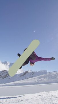 SLOW MOTION: Young pro snowboarder riding the half pipe in big mountain snow park, jumping out of the halfpipe wall and over the sun, performing tricks and rotations with grabs in sunny winter