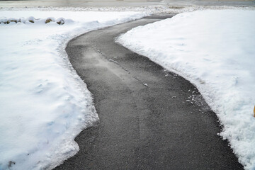 Winding pedestrian sidewalk with snow removed, maintenance of slippery surface in winter