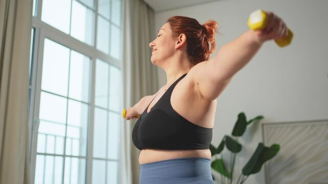 Fitness workout training. Woman picking up dumbbells. Plus size female doing sports exercise at home indoor. Girl in sportswear have workout weight training for weight loss. Sport and fitness