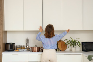 Young woman opening cupboard in kitchen, back view
