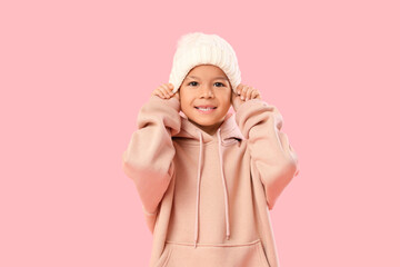 Cute little Asian boy in white knitted hat on pink background