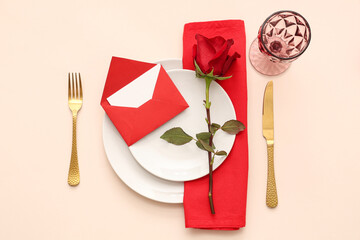 Beautiful table setting with red rose and envelope on beige background. Valentine's Day celebration