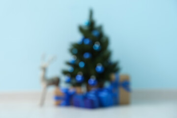 Beautiful Christmas tree with gift boxes and reindeer near blue wall in room. Blurred view