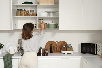 Young woman taking jar from shelf in kitchen, back view