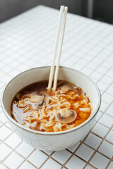 top view of spicy instant noodles with pieces of mushrooms, green red chili peppers and vegetables, spicy ramen noodles on chopsticks in white ceramic bowl. noodle sticks, fast food, hot soup closeup