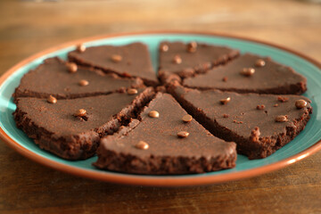 A plate with a chocolate cake, on top little chocolate pieces