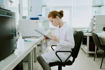 Woman scientist in white coat analyzing data in modern laboratory setting, using a tablet while...