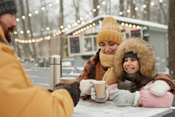 Portrait of happy young family enjoying hot drinks at outdoor cafe table focus on mother and...