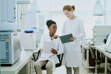 Obraz premium Two scientists engaged in research in modern laboratory, reviewing data and discussing findings. They are surrounded by advanced equipment, indicating high-tech environment