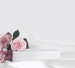 Pink rose flower bouquet on white podium and silk fabric.. Light gray background. Minimal empty display product presentation scene.