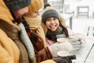 Portrait of happy young girl looking up at mother and father while enjoying hot cocoa at outdoor cafe in winter