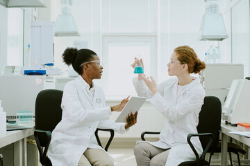 Obraz premium Two scientists discussing an experiment while holding a tablet and beaker in a bright laboratory with advanced equipment present, highlighting teamwork and scientific research
