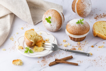 Fresh baked vanilla cinnamon bitten muffin icing sugar powder on retro plate as sweet dessert. Yummy muffins with dessert fork on light marble table background
