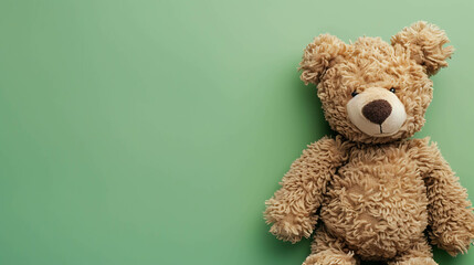 This is a studio shot of a cute and cuddly teddy bear. It is sitting on a green background and looking at the camera with its big, brown eyes.