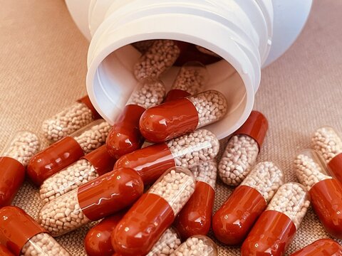 Red and transparent medication capsules pouring from bottle containing pancreatic enzyme