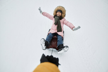 High angle view of cheerful young girl sledding in winter outdoors with fathers hand holding lead,...