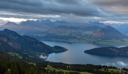 the first morning rays over the lake illuminate the opposite shore of the lake under a cloudy sky - view from the hill