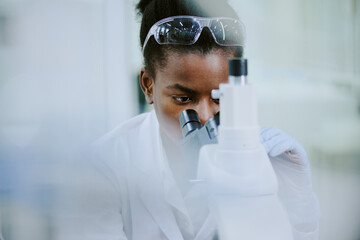 African American female scientist working in laboratory focusing on microscopic examination wearing...