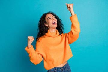 Portrait of nice young girl raise fists wear orange sweater isolated on turquoise color background