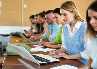 Fototapeta premium Portrait of a young girl student studying with fellow students in a university auditorium during classes on a laptop and ..writing a synopsis in a copybook