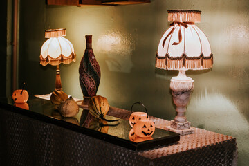 Two vintage lamps with fringed shades illuminating a table decorated with Halloween-themed items,...