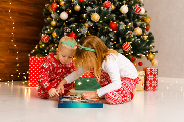 Brother and sister in cozy pajamas are curiously looking at a Christmas gift.