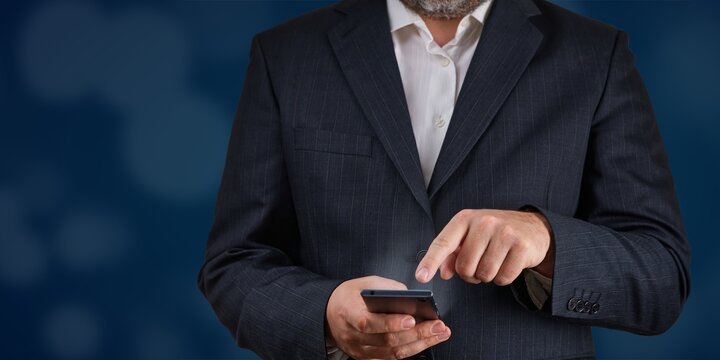 A confident businessman in a tailored suit is using a smartphone against a dark blue background. This image symbolizes modern technology, effective communication, and a dynamic mobile lifestyle. - Powered by Adobe