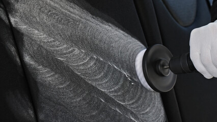 Professional car cleaning. Worker uses professional brush tool to clean car seat upholstery leaving...