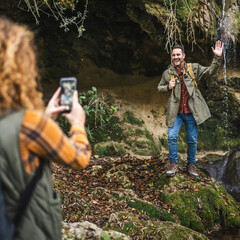 wife take a photo of husband backpacker in front cave in the forest