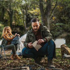 Adult man hiker kneel and start a fire with paper ready for camping