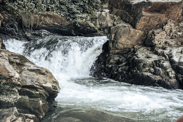 Water flows gracefully over rugged stones, creating a beautiful waterfall surrounded by vibrant foliage, embodying a peaceful morning atmosphere.
