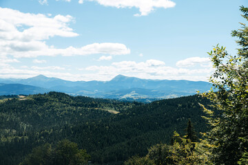 Fototapeta premium A breathtaking view of rolling green hills and distant mountains under a vibrant blue sky, capturing the serene beauty of nature in the early afternoon
