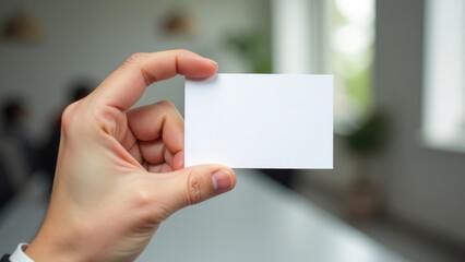 A hand is holding up a blank business card in an office environment. Concept of business card mockup 