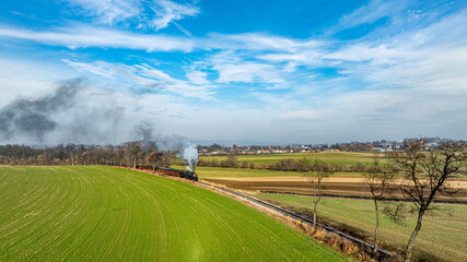 Steam Train Traverses Lush Green Fields Under a Bright Blue Sky in Early Autumn Afternoon