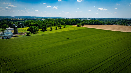 Lush green fields stretch across the landscape, dotted with trees and a white barn. A clear blue sky enhances the serene rural setting on a sunny day.