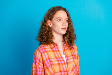 Young redhaired woman in bright plaid shirt posing against vibrant blue backdrop