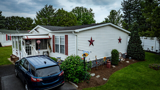 A cozy single-story house features decorative stars on the exterior, surrounded by a vibrant garden. A dark blue vehicle is parked in the driveway, with greenery enhancing the peaceful atmosphere.