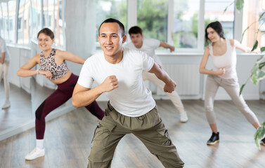 Enthusiastic smiling young Asian man in activewear energizing group during dance fitness class in...