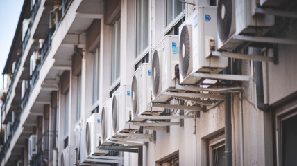 A row of air conditioners are mounted on the side of a building. The air conditioners are all the same size and are evenly spaced