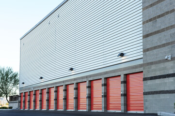 A row of exterior storage units with red roll-up doors lines the side of a modern self-storage...