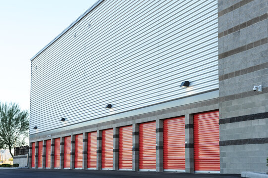 A row of exterior storage units with red roll-up doors lines the side of a modern self-storage facility, featuring secure access and durable construction for residential or commercial use