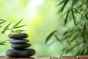 Zen stone stack with bamboo leaves on wooden table, serene spa concept banner with green background and ample copy space, capturing tranquility in boho style with smooth natural light.