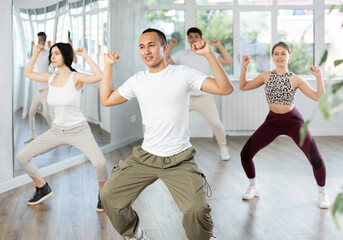Expressive Asian guy honing hip-hop dance moves in mirrored choreographic studio setting during...