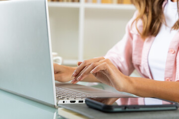 Woman typing on laptop at home, smartphone nearby on desk